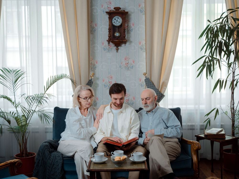 An older couple and a younger family member looking through a photo album together on a sofa