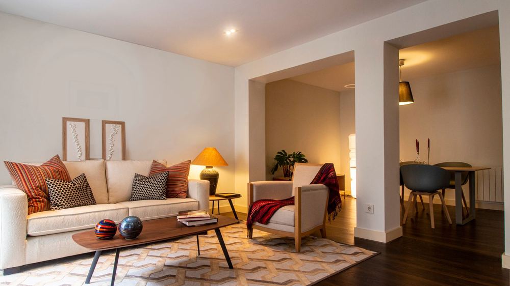 A warm, softly lit living room with a sofa, cushions, and lamps