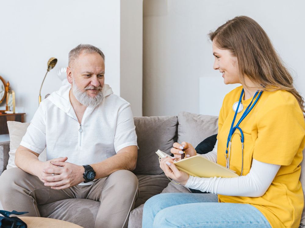 A nurse and an older man talking comfortably on a couch at home